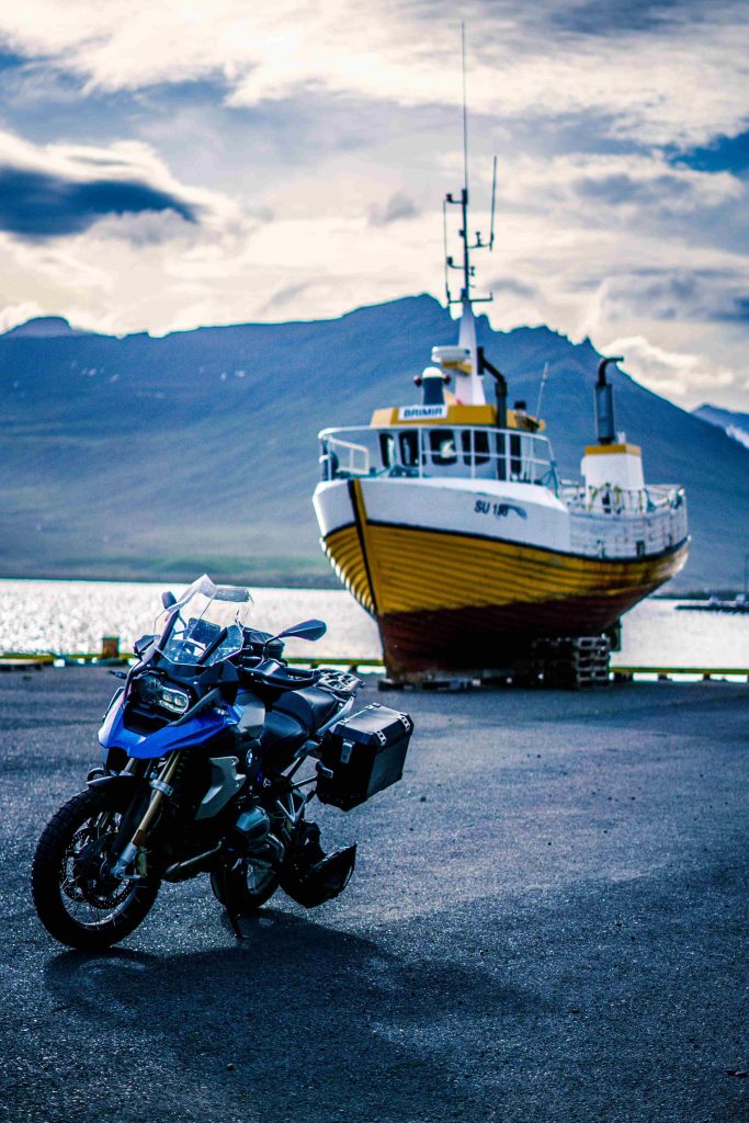 BMW GS 1250 Motorrad vor einem alten, schönen Boot in einem kleinen Hafen im Süden Islands während unserer Motorradtour 2022